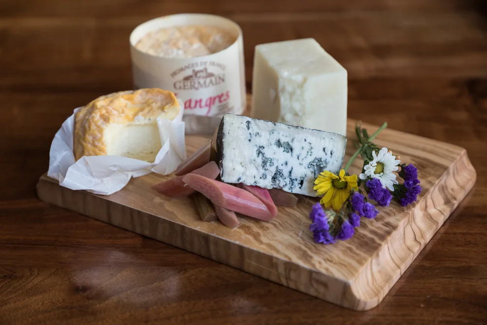 A cheese board with blue cheese, Langres and a hard cheese on an olive wood board