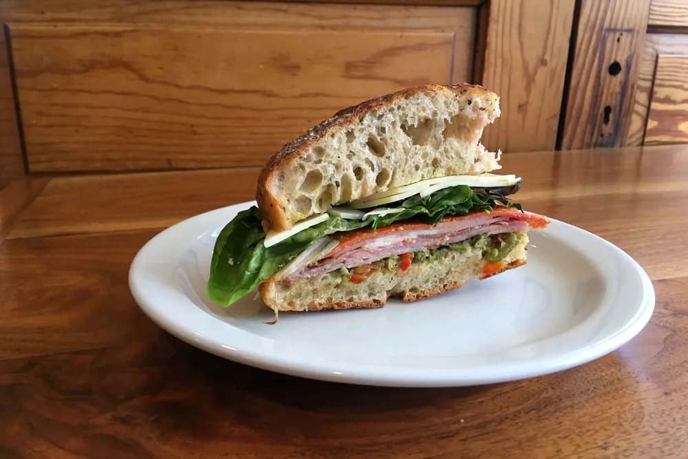 A sandwich on house bread with ham, salami, cheese and greens